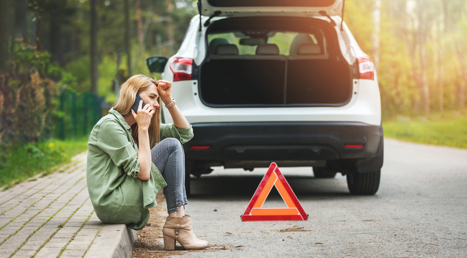 A woman on the phone and sitting on the curb after a car accident